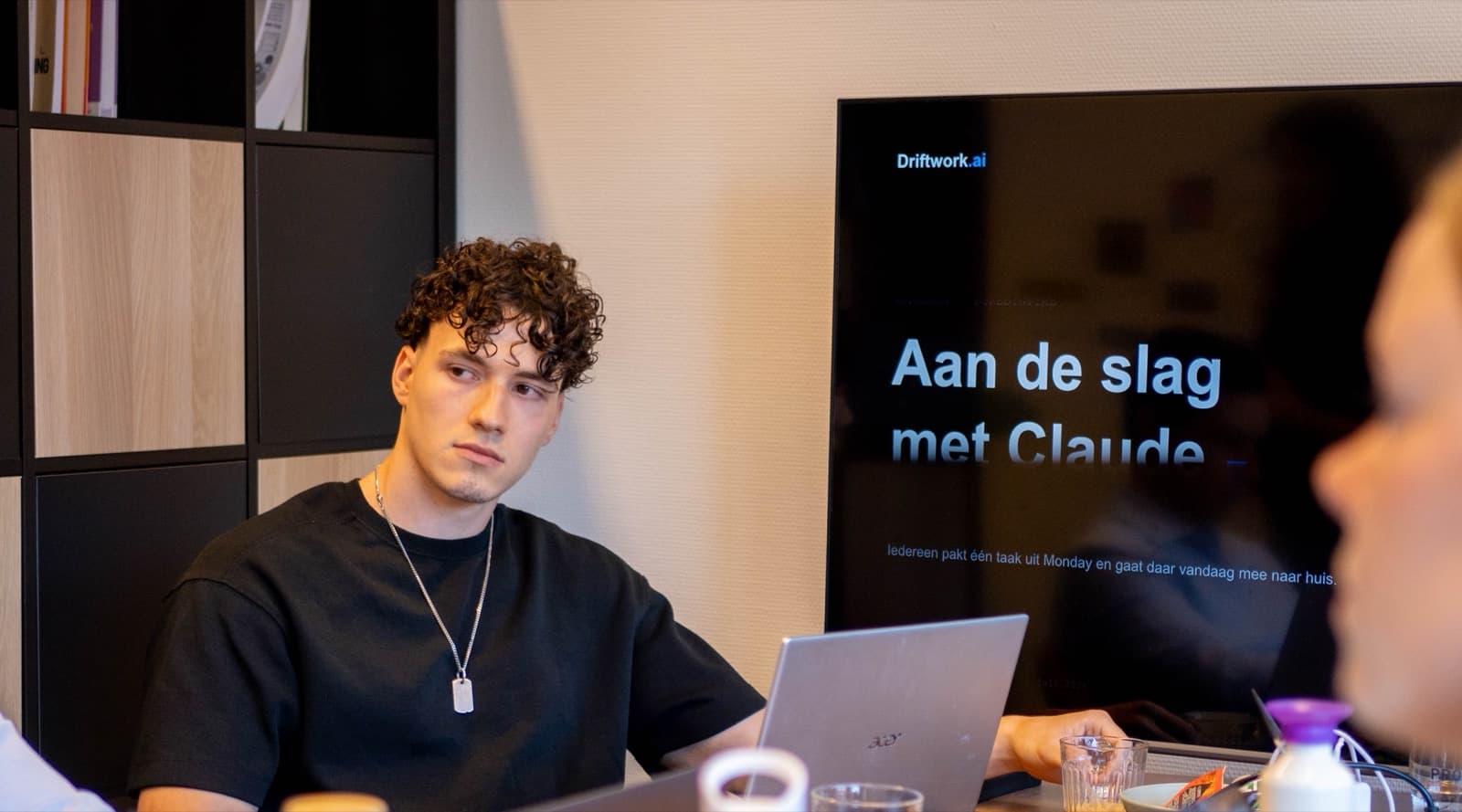 Deelnemers aan tafel met open laptops tijdens de sessie bij Pure Digital. Op het scherm achter hen de slide met de opdracht om één eigen taak te pakken en die dezelfde dag af te maken.
